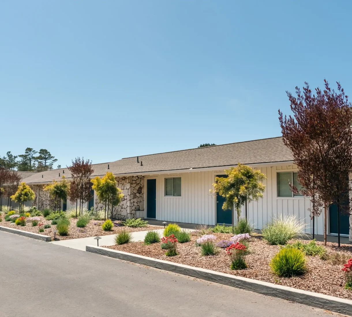 Row of guest rooms with stone accents and garden at Fort Bragg hotel