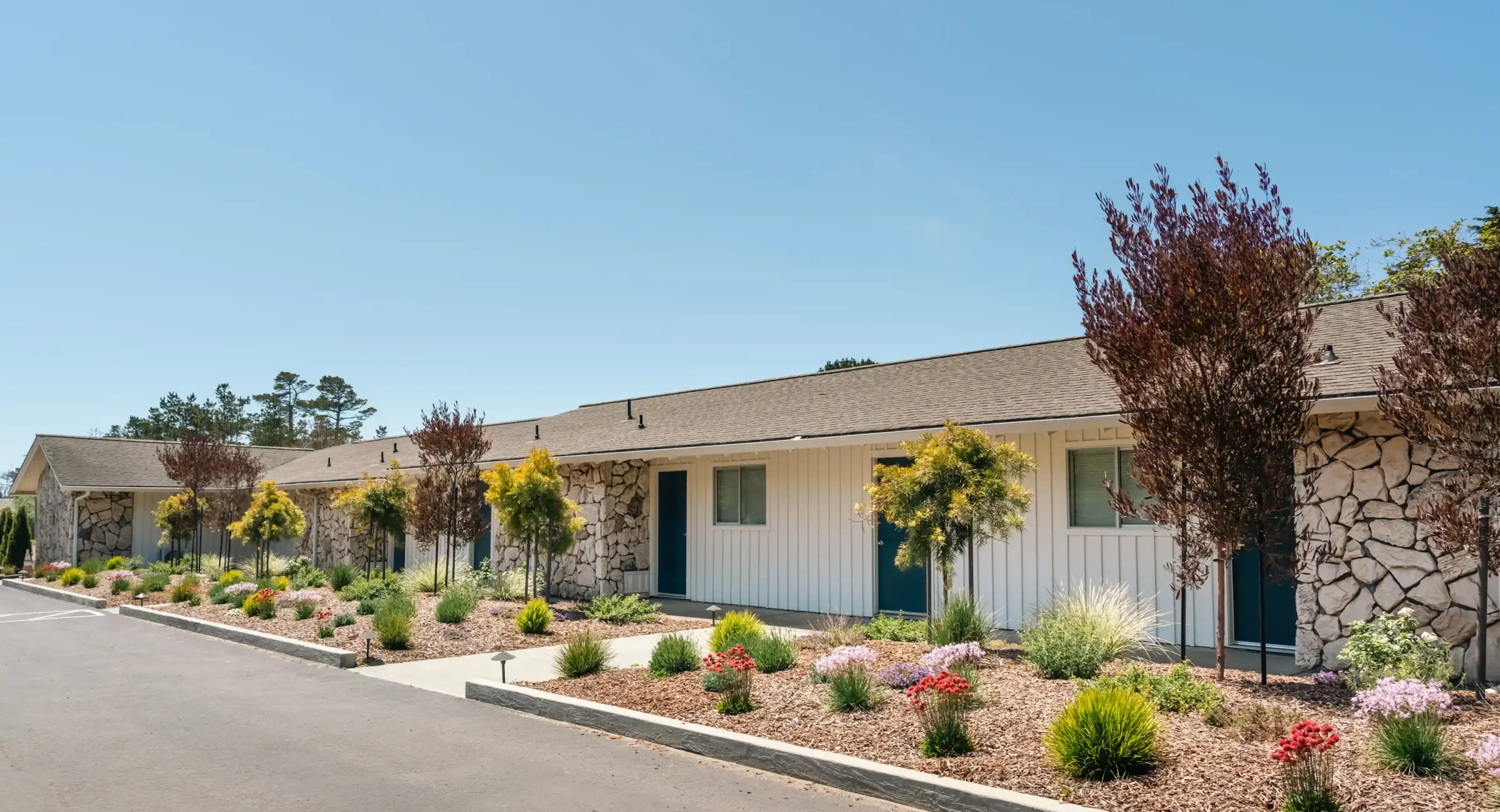 Row of guest rooms with stone accents and garden at Fort Bragg hotel