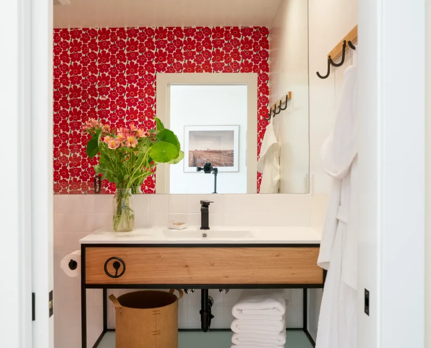 Bathroom vanity at Mendocino coast hotel with wood sink cabinet, mirror, and floral red tile wall